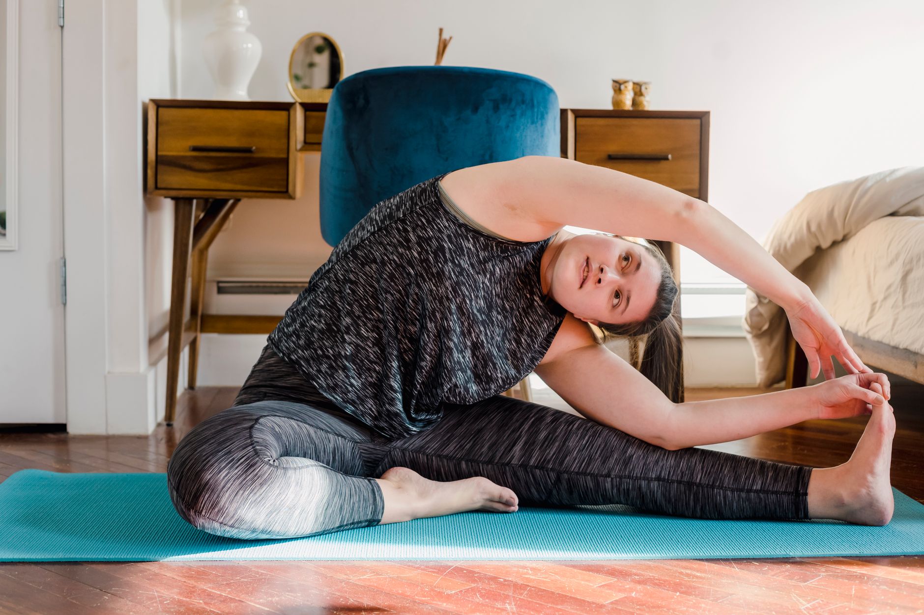 Femme assise sur un tapis turquoise qui étire sa jambe tendue