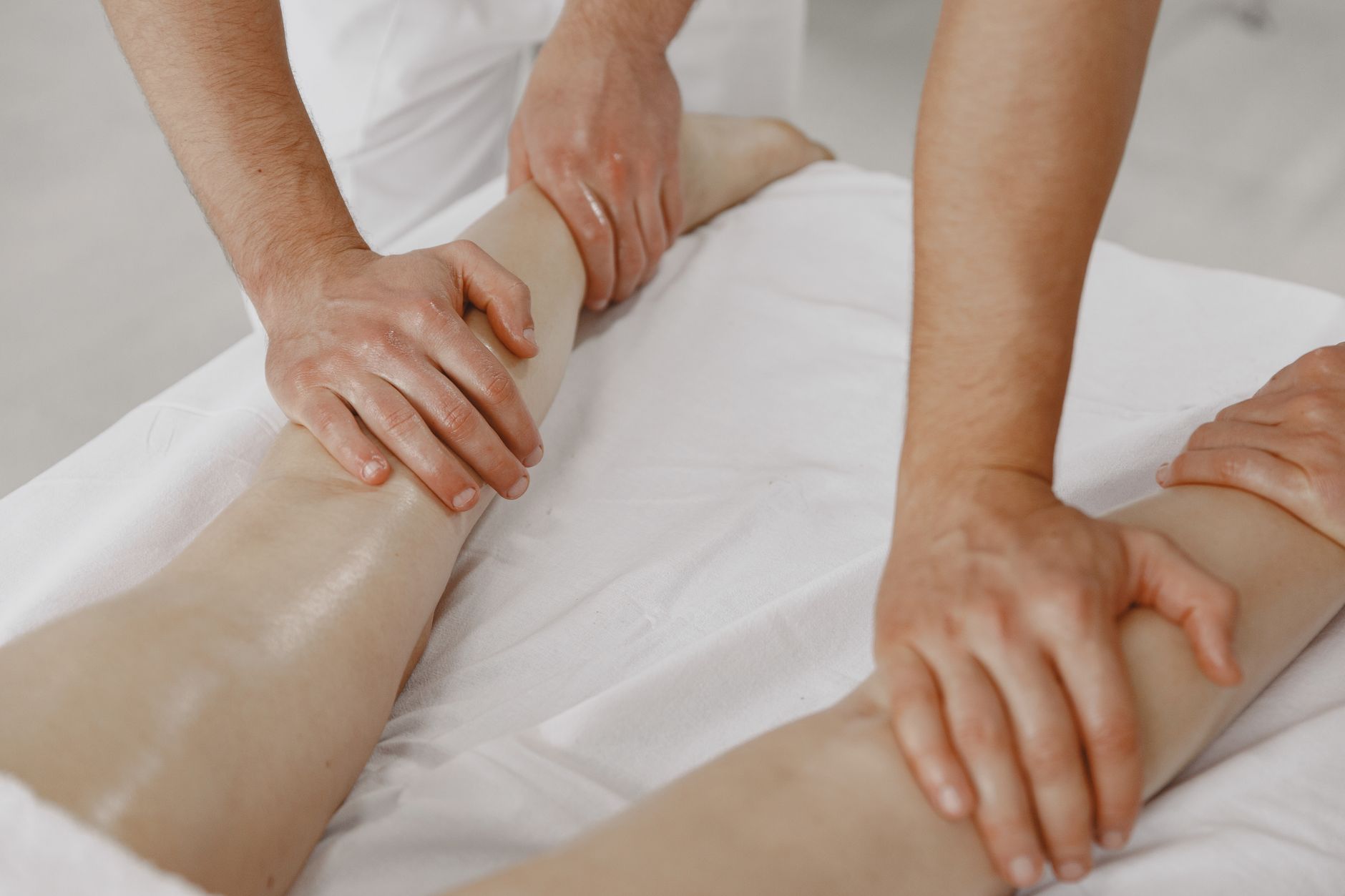 Mains qui massent les jambes d’une personne allongée sur une table de soin
