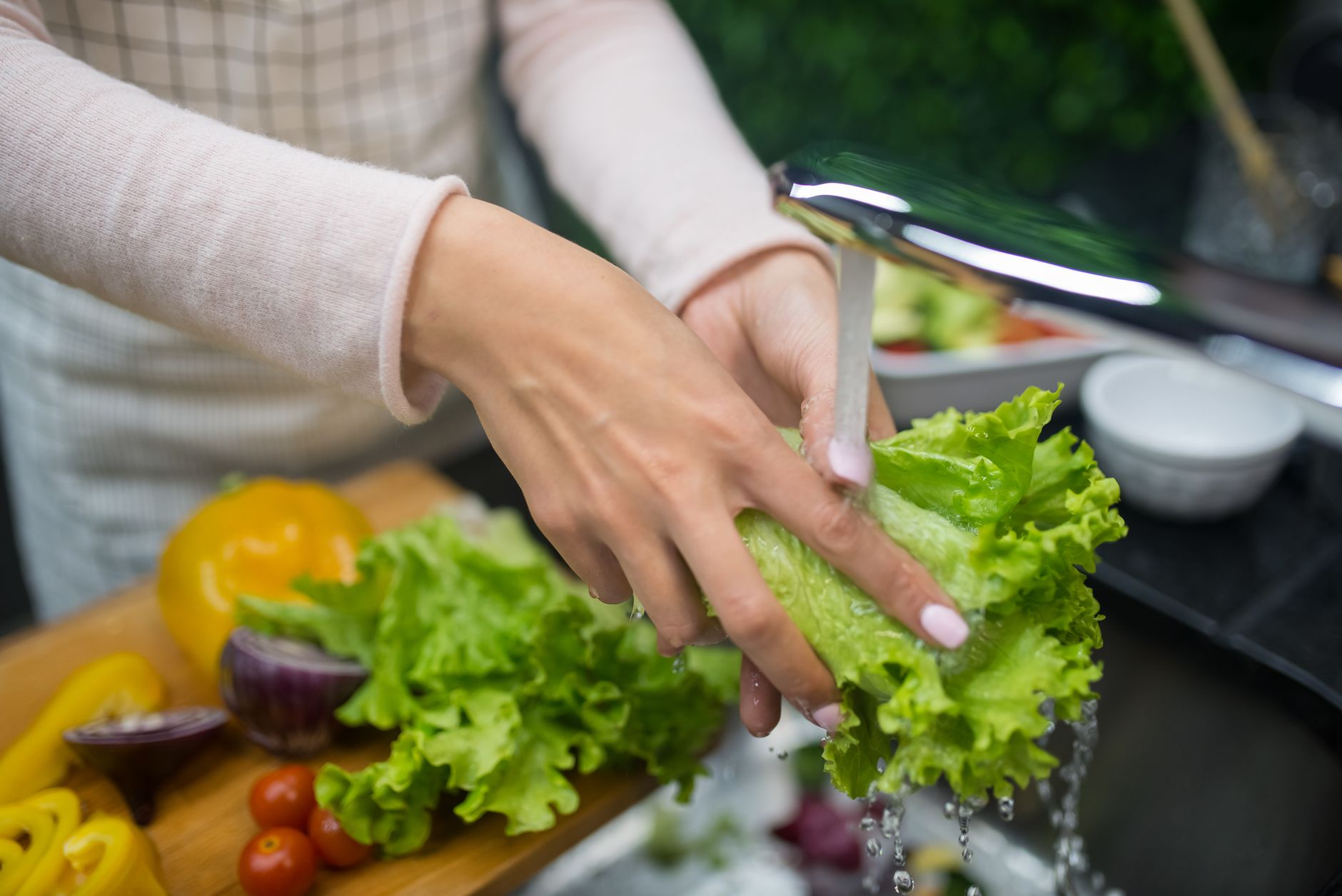 Mains qui rincent une salade sous le robinet, poivrons et tomates à côté