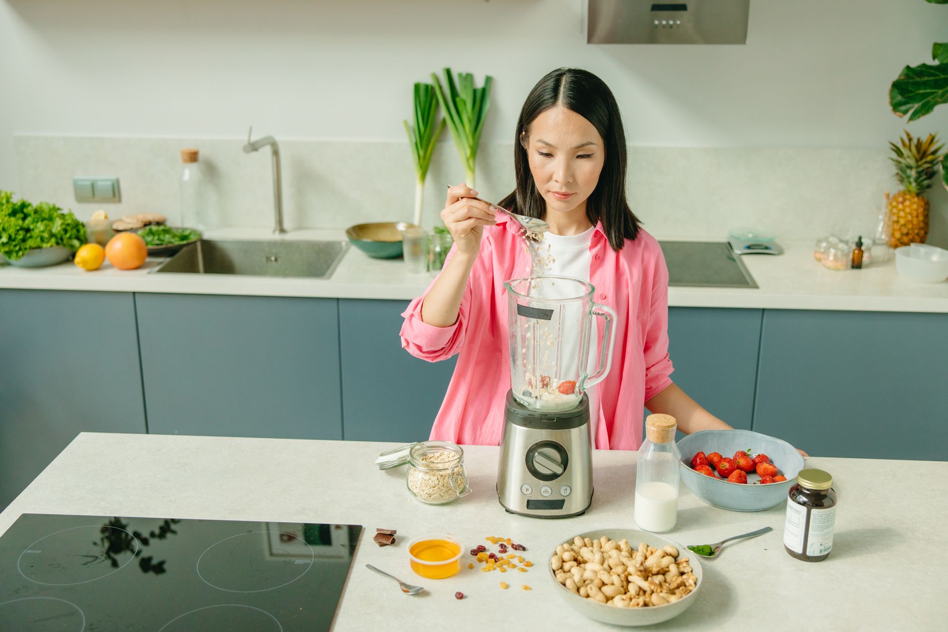 Femme en chemise rose qui prépare un smoothie dans une cuisine claire