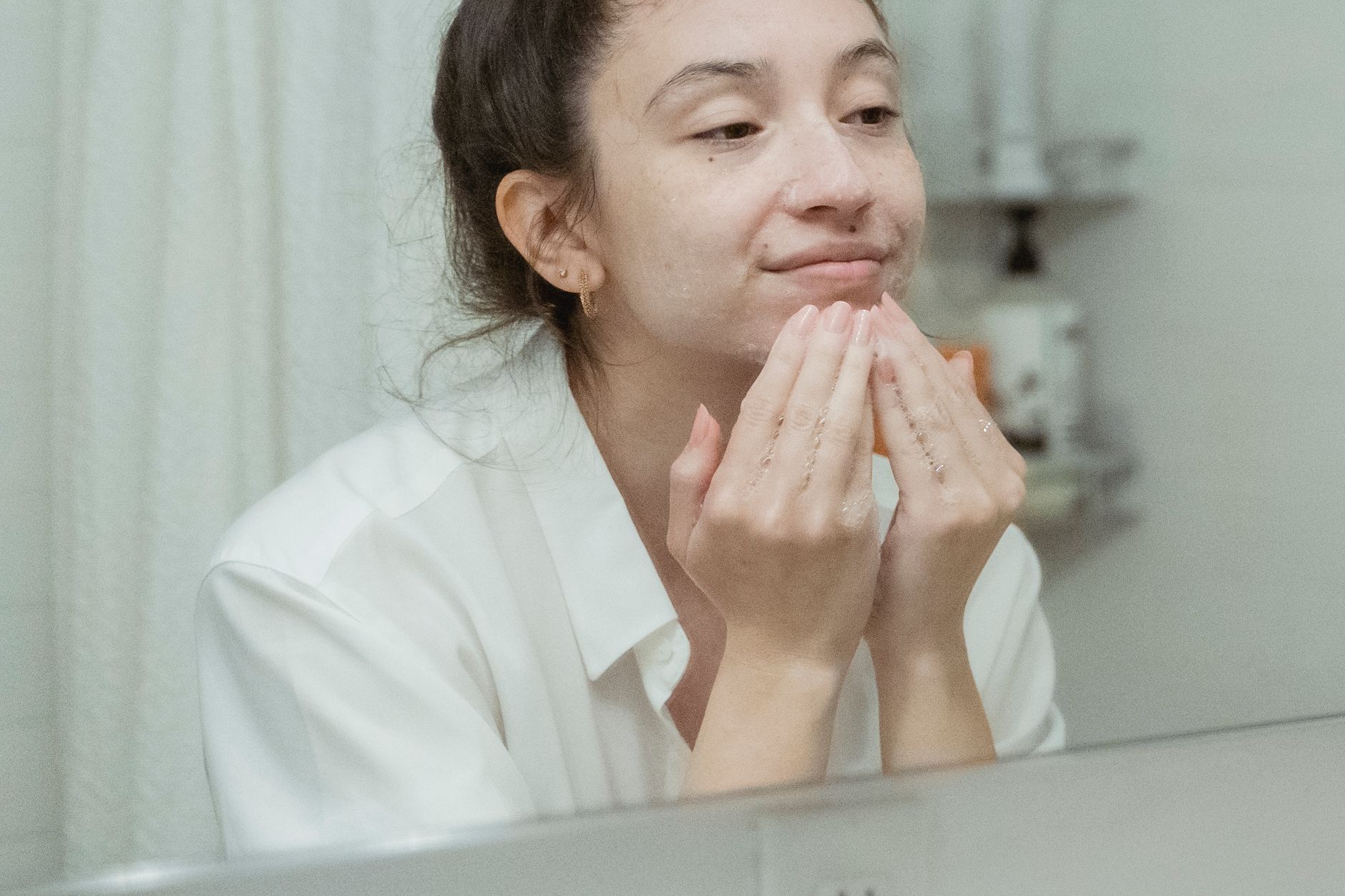 Jeune femme en chemise blanche qui se masse les joues devant un miroir