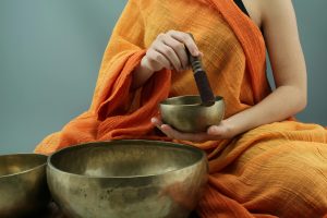 Una persona con vestimenta tradicional utiliza cuencos tibetanos durante una práctica meditativa.