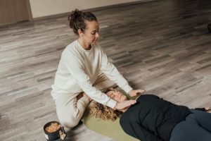 Mujer practicando terapia curativa Reiki a otra mujer tumbada en el interior sobre una esterilla de yoga.