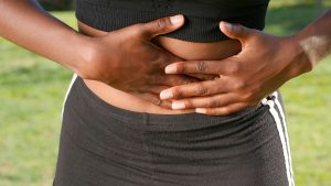 Una mujer se sujeta el vientre hacia fuera, lo que indica posibles molestias o dolores abdominales.