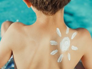 Enfant avec de la crème solaire en forme de soleil dans le dos, profitant d'une journée ensoleillée près de la piscine.