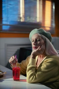 Une femme âgée portant un béret profite d'une boisson fraîche avec une paille à l'intérieur, reflétant loisir et détente.