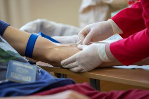 Medical professional drawing blood from donor's arm in a clinical setting. Professionnel de santé prélevant du sang sur le bras d'un donneur dans un cadre clinique.