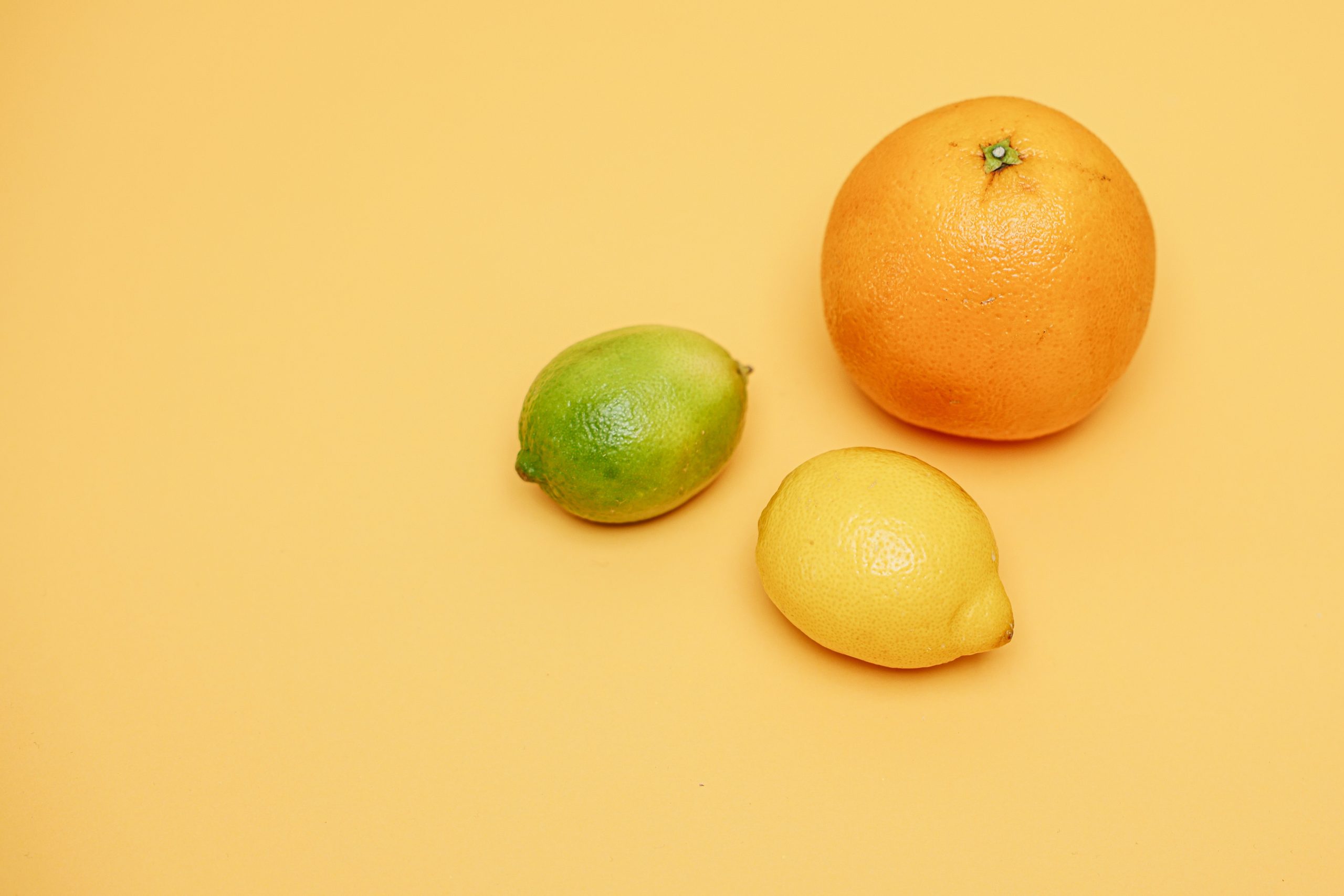 Close-up of lemon, lime, and orange on a yellow surface, showcasing fresh organic citrus fruits. Gros plan de citron, citron vert et orange sur une surface jaune, mettant en valeur des agrumes biologiques frais.