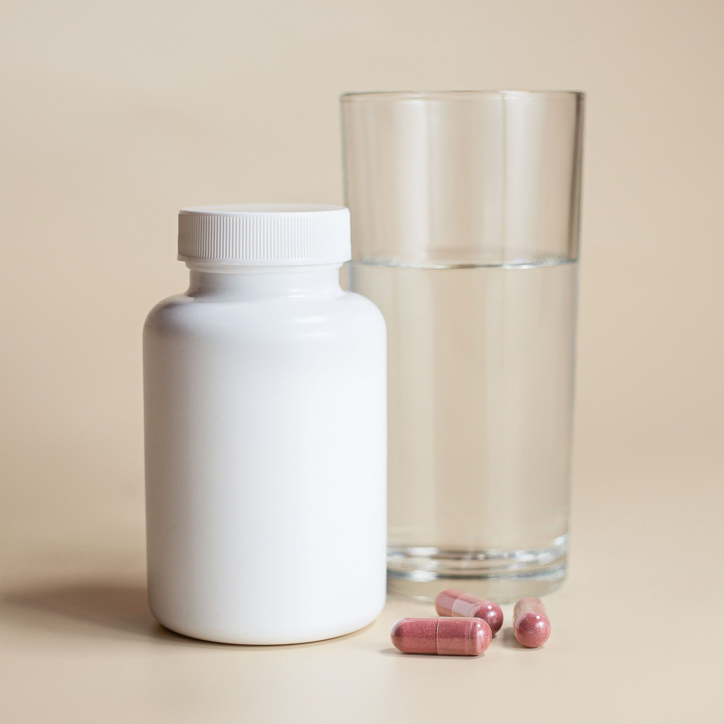 White supplement bottle with capsules and a glass of water on a neutral background. Bouteille de supplément blanc avec des capsules et un verre d'eau sur un fond neutre.