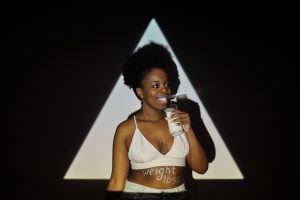 Femme souriante tenant un verre de lait devant un fond d'ombre triangulaire, suggérant un concept de perte de poids.