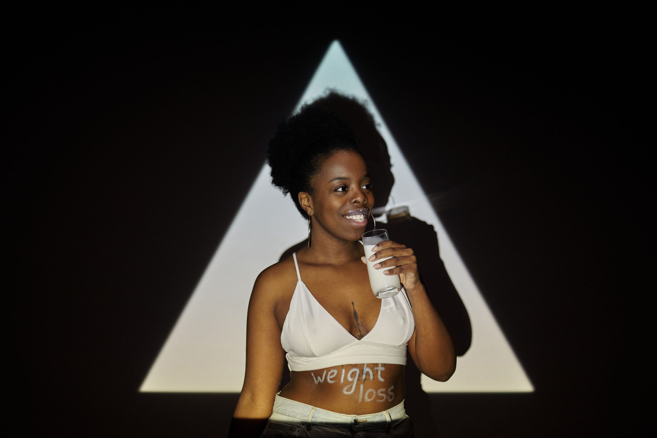 Femme souriante tenant un verre de lait devant un fond d'ombre triangulaire, suggérant un concept de perte de poids.