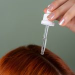 Close-up of applying serum to roots with a precision dropper on red hair, showcasing hair care routine. Gros plan sur l'application d'un sérum sur les racines avec un compte-gouttes de précision sur cheveux roux, mettant en avant la routine de soin des cheveux.