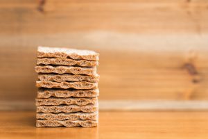 A neatly stacked pile of crispbread sits on a wooden surface with a blurred wooden backdrop. Une pile bien rangée de pain croustillant repose sur une surface en bois avec un fond en bois flou.