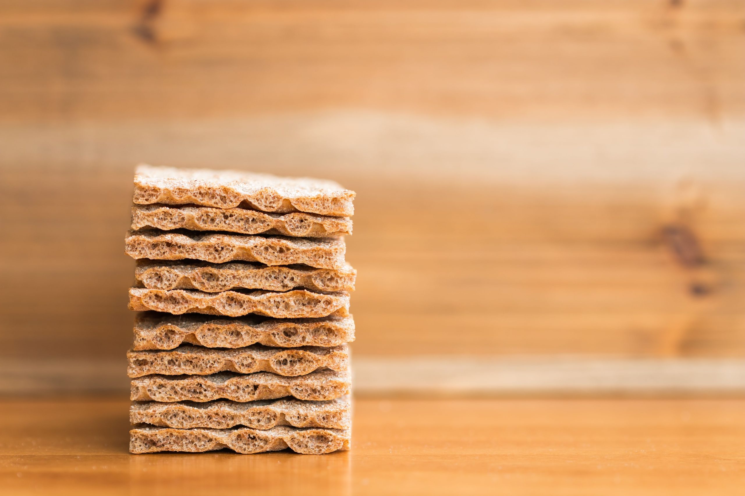 A neatly stacked pile of crispbread sits on a wooden surface with a blurred wooden backdrop. Une pile bien rangée de pain croustillant repose sur une surface en bois avec un fond en bois flou.