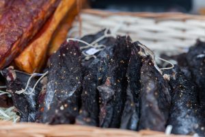 A close-up view of dried, seasoned meat slices displayed in a wicker basket. Une vue rapprochée de tranches de viande séchée et assaisonnée exposées dans un panier en osier.
