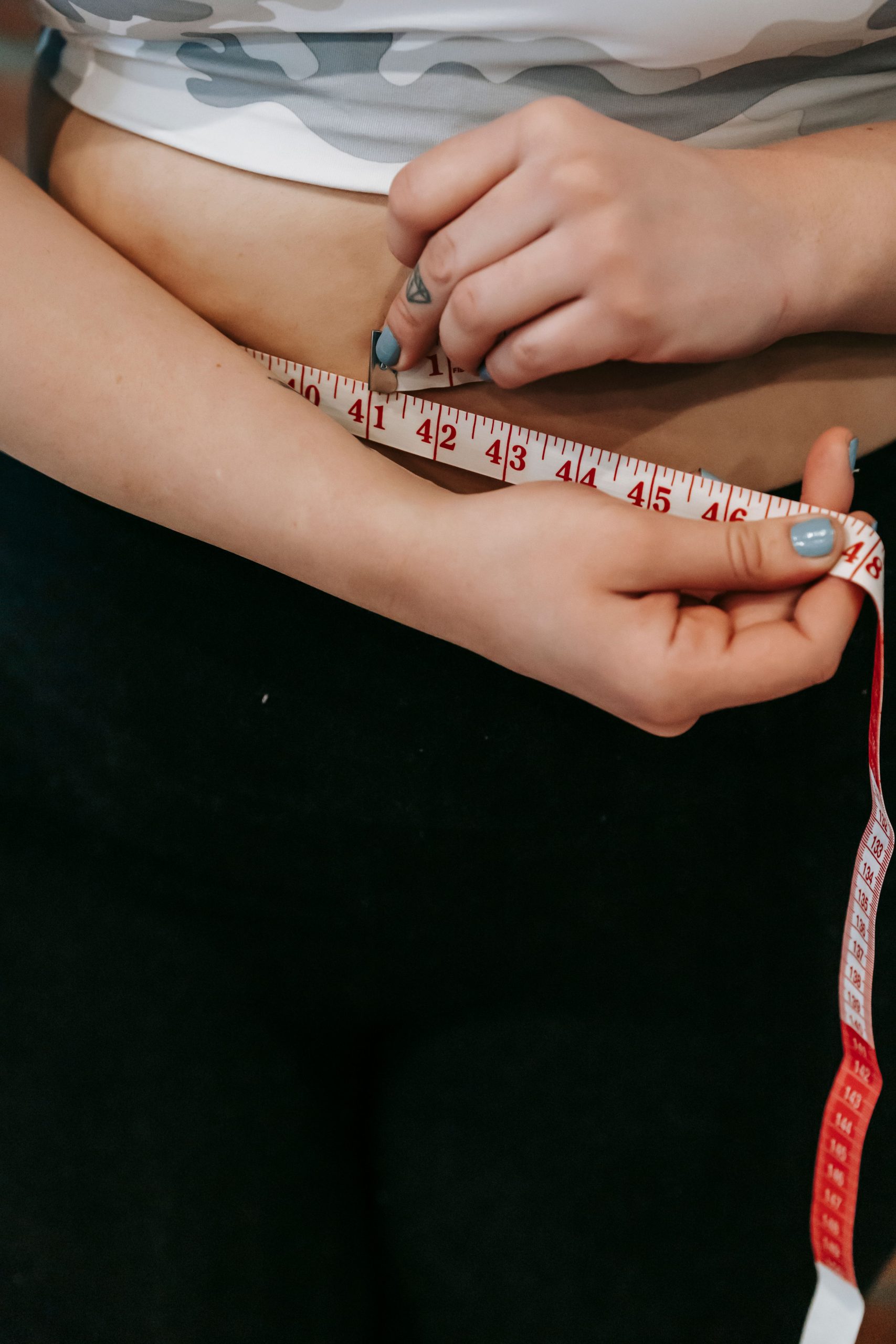 High angle of crop faceless overweight female measuring waist with centimeter for weight loss Vue de haut d'une femme en surpoids sans visage mesurant sa taille avec un centimètre pour la perte de poids