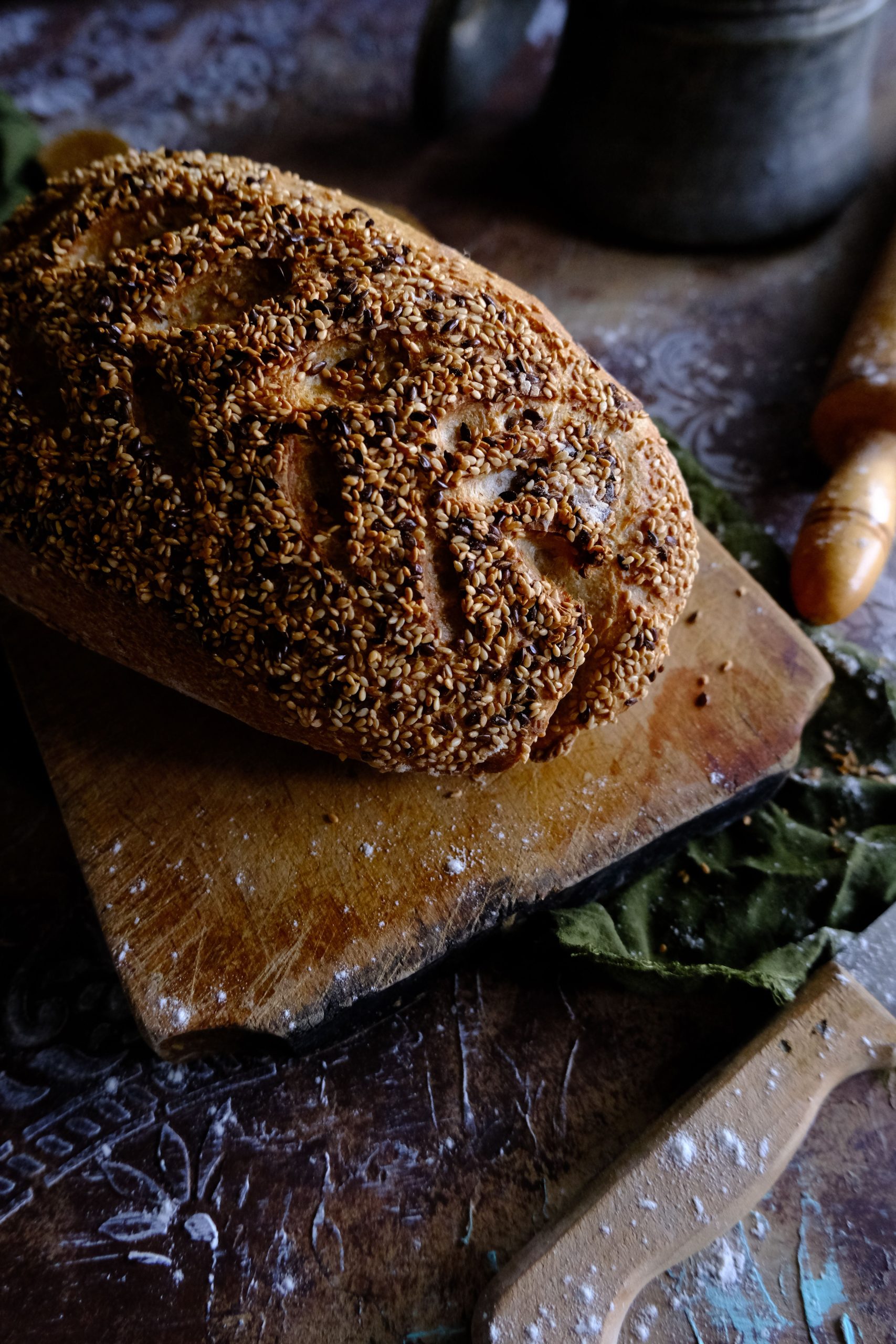 Freshly baked artisan bread with sesame seeds on a wooden board, evoking a homely baking atmosphere. Du pain artisanal fraîchement cuit avec des graines de sésame sur une planche en bois, évoquant une atmosphère de cuisson chaleureuse.