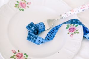 A floral plate with a fork and blue measuring tape symbolizing dieting or healthy eating. Une assiette florale avec une fourchette et un ruban à mesurer bleu symbolisant un régime ou une alimentation saine.