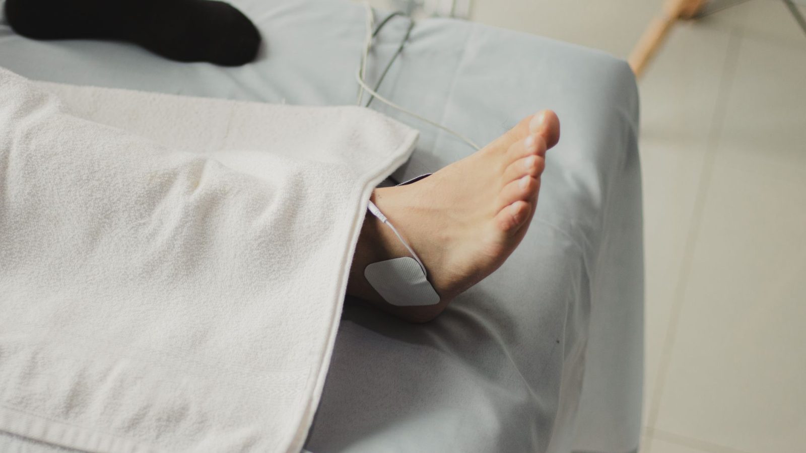 Électrode d’électrostimulation posée sur la cheville d’une personne allongée sur une table de soin, jambe sous une serviette